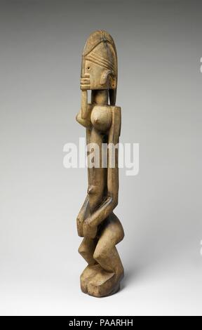 La figura: femmina (Dege Dal Nda). Artista: Maestro di Ogol. Cultura: popoli Dogon. Dimensioni: H. 25 x W. 3 3/4 x D. 4 7/8 in. (63,5 x 9,5 x 12,4 cm). Data: XVIII-XIX secolo. Questa figura femminile è uno dei circa una dozzina di opere che sono state attribuite allo stesso artista Dogon, identificata da storici dell'arte come il Maestro di Ogol dopo un villaggio nella regione di Sanga dove un lavoro in questo corpus è stato raccolto nel 1935. La forma della testa e le caratteristiche facciali di opere create dal Master si distinguono per la testa helmetlike e l unica impilate orizzontalmente bocca-narici-mento ensemble, strettamente f Foto Stock