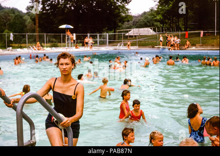 Donna che indossa un pezzo di costume da bagno che arrampica una scala fuori di una piscina occupata, Briarcliff Manor locale piscina, Westchester County, New York, Stati Uniti negli anni '60 Foto Stock