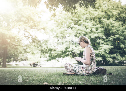 Donna che utilizza lo smartphone nel parco pubblico Foto Stock