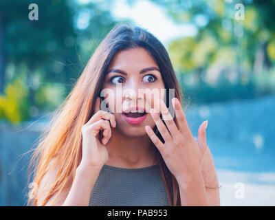 Sorpreso ragazza ascoltato notizie sorprendenti sul telefono. Gossip con la fidanzata. La donna parla sullo smartphone. Bella imprenditrice sulla strada. Emozioni, concetto tecnologico. Foto Stock