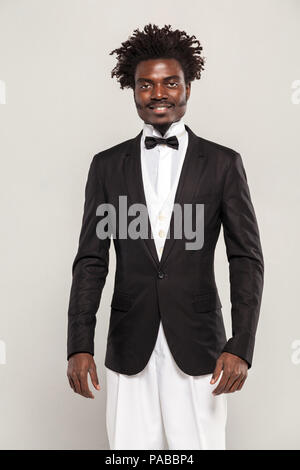 Riccamente gentelman africana con afro stile di capelli in stile classico smoking e farfallino sorridente. Indoor, isolato studio shot su sfondo grigio Foto Stock