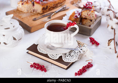 Tazza di tè e caffè e piattino, tortina con ribes rosso sul pannello di legno e sfondo bianco, fiori di cotone Foto Stock