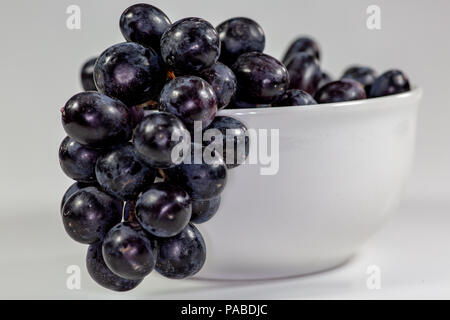 Uva nera in una profonda coppa bianco su un racconto bianco in attesa di essere consumati Foto Stock