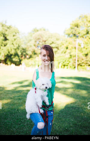 Ritratto di bella non valido sorridente ragazza nata senza arti superiori godendo con il suo piccolo cucciolo bianco nel parco. Foto Stock