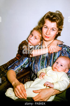 Ritratto di famiglia di madre e due figli negli Stati Uniti negli anni '60. La giovane donna ha capelli biondi e indossa rossetto rosso. La bambina bionda di 4 anni abbraccia la madre. La madre sta tenendo un bambino in un vestito giallo di sonno Foto Stock