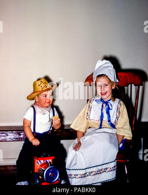 Bambini piccoli in costume da vestito fantasia per Halloween negli Stati Uniti negli anni '50. La bambina di quattro anni indossa un costume tradizionale olandese e il bambino indossa un cappello e un fazzoletto seduto su un motore giocattolo Foto Stock