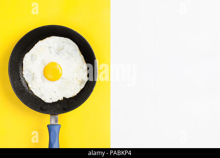 Fresco uova cotte in padella su split di colore giallo e sfondo bianco, laici immagine piatta. Foto Stock