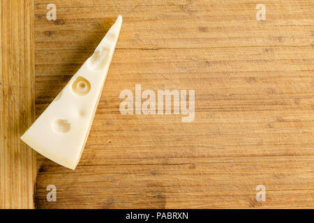 Cuneo tradizionali olandesi Maasdam formaggio con fori su un vecchio di bambù in legno tagliere con spazio copia pronto a tagliare e servire Foto Stock