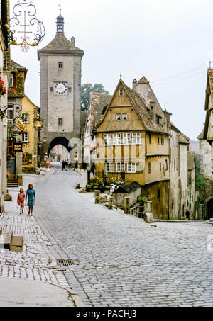 Vecchia strada acciottolata all'ingresso della torre dell'orologio della città medievale di Rothenburg ob der Tauber, Ansbach, Franconia centrale, Baviera, Germania con case a graticcio negli anni '60 Foto Stock