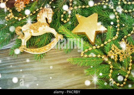 Sfondo di natale con un cavallo giocattolo, stella d'oro, verde abete rami e altre decorazioni su vecchie tavole di legno Foto Stock