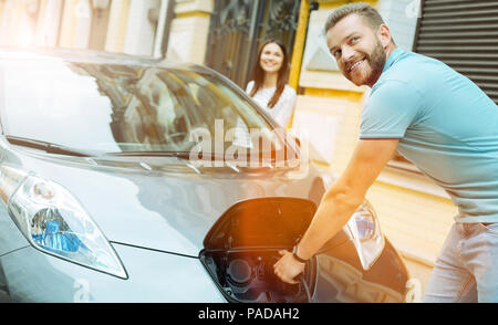 Giovani carino coppia la carica di un auto elettrica mentre si è in viaggio Foto Stock