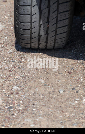 Un pneumatico di gomma di una vettura in un paese strada di ghiaia mentre si guida in campagna, un close-up di una parte della strada e un auto Foto Stock