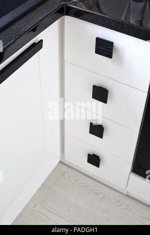 Soluzione per un angolo cottura per lo storage in un armadio. Una unità di angolo con scaffali e cassetti con quadrato nero manici in legno bianco e rovere spazzolato pan Foto Stock