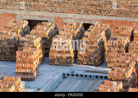 Close-up le pile di mattoni rossi ordinatamente accatastati sulle fondamenta in calcestruzzo del seminterrato o al primo piano della casa in futuro per la costruzione di pareti su soleggiate giornate estive Foto Stock