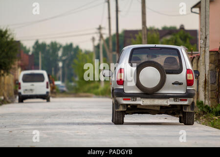 Vista posteriore del nuovo argento lucide costosa auto SUV parcheggiato sulla strada asfaltata lato a cottage in pietra sul recinto luminoso sfocato soleggiato verde residenziale suburbana Foto Stock