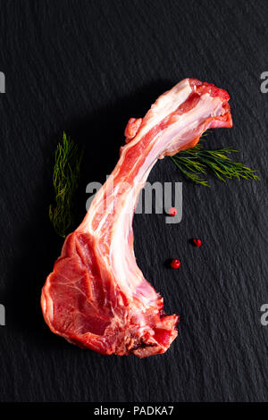 Concetto di cibo organico costolette di agnello su ardesia nera pietra con erbe Foto Stock