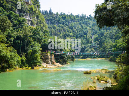 Bellissima scena di foresta, al fiume e al ponte di sospensione in Cina Guizhou Huangguoshu scenario park. Foto Stock