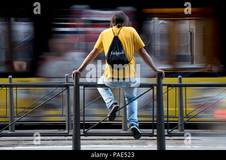 Belgrado, Serbia - Luglio 12, 2018 : Una casual medioevo uomo seduto sulle ringhiere in attesa ad una fermata degli autobus per il trasporto pubblico con sfocata mot Foto Stock