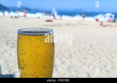 Un grande bicchiere di birra fresca con sfocati spiaggia di Copacabana è pieno di gente in background, Rio de Janeiro, Brasile Foto Stock