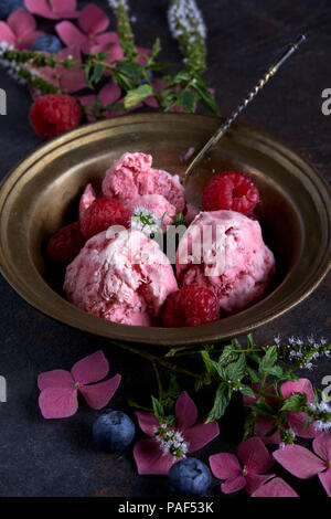 In casa gelato al lampone nel recipiente di rame sul tavolo con bacche e fiori da giardino. Foto Stock