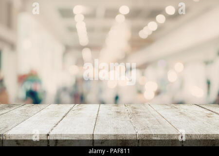 Svuotare tavolo in legno e sfondo sfocato - Store di shopping mall blur sullo sfondo bokeh con display montage per prodotto. Foto Stock