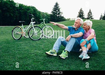 Positivo vecchia coppia si siede sul prato, con le loro biciclette Foto Stock