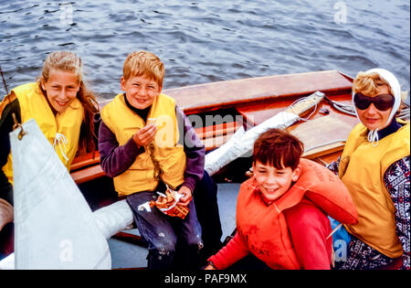 Famiglia di una donna e tre bambini che indossano giubbotti salvagente in una piccola barca a vela sul fiume Helford, Cornovaglia, Inghilterra, Regno Unito negli anni '60. Foto Stock