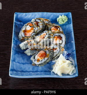 Rotoli di sushi su una piastra con salmone e cetrioli su un tavolo di legno. Foto Stock