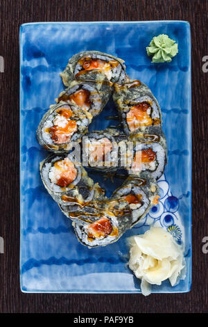 Rotoli di sushi su una piastra con salmone e cetrioli su un tavolo di legno. Foto Stock