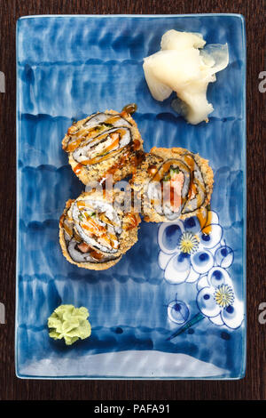 Fritti caldi sushi rotoli su una piastra con salmone e cetrioli su un tavolo di legno. Foto Stock
