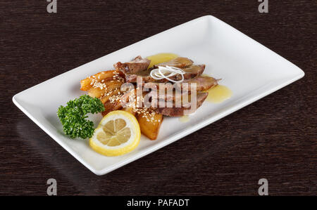 Pezzi di carne con la salsa a base di patate arrosto e una fettina di limone e prezzemolo sulla piastra bianca. Cucina Europea. Vista laterale Foto Stock