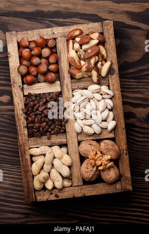 Vari dadi selezione: arachidi, nocciole, castagne, noci, pistacchi e le noci pecan in una scatola di legno. Vista superiore Foto Stock