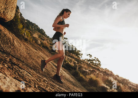 donna sportiva che corre in discesa su un sentiero roccioso di montagna. Atleta di trail runner che si allena per una corsa in discesa. Foto Stock