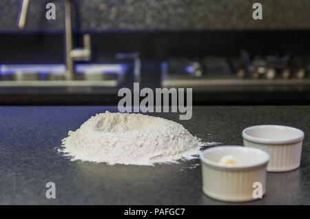 Cumulo di farina di grano sulla sommità del granito nero del tavolo, preparazione di impasto per pizza. Foto Stock