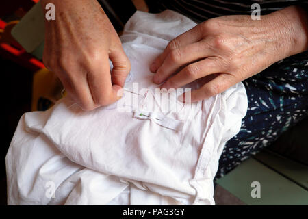 Close-up di una donna anziana con le mani in mano la riparazione di rammendo un foglio di cucitura bianco con nastro di cotone Wales UK KATHY DEWITT Foto Stock