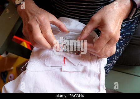 Primo piano di una donna anziana che ripara le mani minacciando una lacerata foglio cucito con nastro di cotone bianco che tiene una scatola di Pins in Galles UK KATHY DEWITT Foto Stock