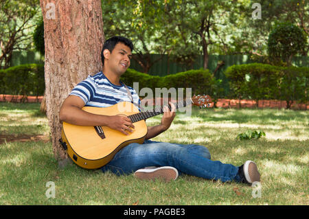 Giovane uomo suonare la chitarra sotto agli alberi Foto Stock