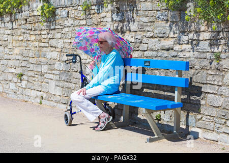 Bournemouth Dorset, Regno Unito. Il 23 luglio 2018. Regno Unito: meteo canicola continua Come temperature aumento su una cocente sole e caldo giorno a Bournemouth spiagge con un cielo azzurro e sole ininterrotta. Sunseekers in testa al mare a prendere il sole. Senior donna seduta da sola sulla passeggiata sotto un ombrello che offre una certa protezione dal calore. Credito: Carolyn Jenkins/Alamy Live News Foto Stock