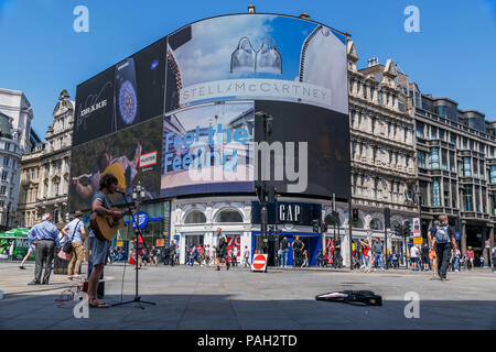 Un suonatore ambulante è suonare la chitarra accanto alla statua di Eros a Piccadilly Circus, Londra,2018. Foto Stock