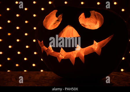 Funny arancione zucca come una testa con occhi scolpiti e un sorriso su uno sfondo nero con una ghirlanda di fiori per la festa di Halloween Foto Stock