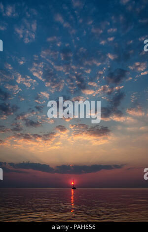 Il sole scende tra le onde del mare contro lo sfondo di yacht e nuvole all'orizzonte Foto Stock