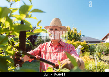 Ritratto di un allegro attivo uomo senior arbusti di trimming in giardino Foto Stock