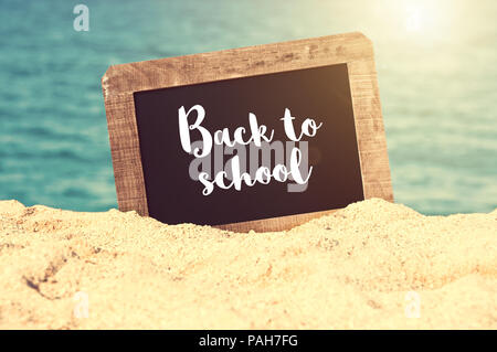 Si torna a scuola scritto su una lavagna vintage nella sabbia di una spiaggia Foto Stock