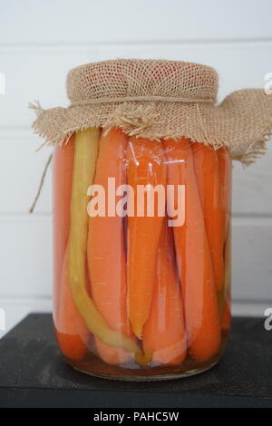 Le carote con spezie nel vasetto di vetro. Vaso di vetro con le carote su nero scaffale di legno Foto Stock