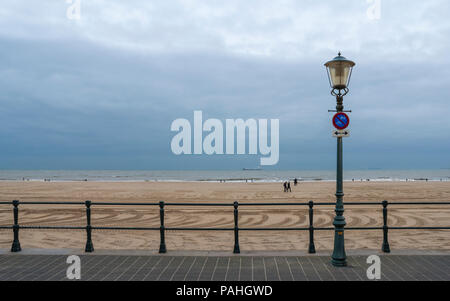 Vista di una spiaggia deserta nel fuori stagione, con un lampione e corrimano su una spianata in primo piano. Scheveningen, l'Aia, Paesi Bassi Foto Stock