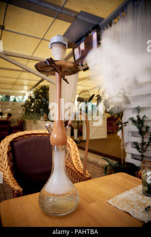 Hookah con una nuvola di fumo su un tavolo in un ristorante estivo. Foto Stock