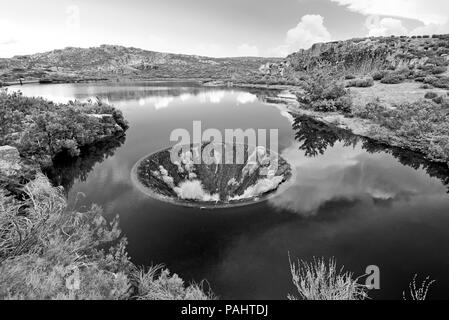 L'uomo ha fatto imbuto nel mezzo di un lago di montagna in bianco e nero Foto Stock