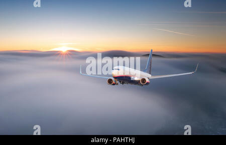 Aereo passeggeri. Paesaggio con grande bianco aereo è volare nel cielo rosso sopra le nuvole e il mare al tramonto colorato. Aerei per il trasporto di passeggeri è landi Foto Stock