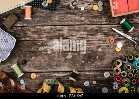 Bellissimo set di sparsi in ruvida tavola di legno metallo forbici, pulsanti assortiti e la cucitura di steli con i fili colorati e nastro di misurazione da ab Foto Stock