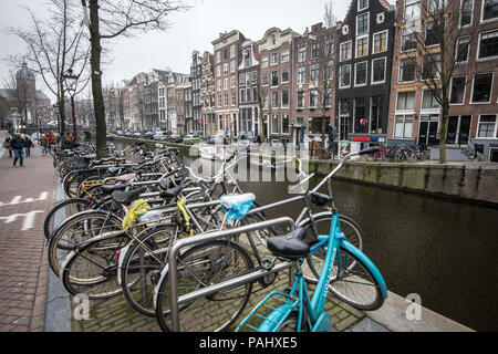 Incatenato biciclette a riposo lungo il lato del canal che corre attraverso la città di Amsterdam, Paesi Bassi. Foto Stock